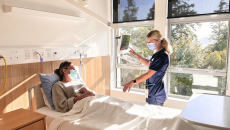 A nurse talking to a patient while using Rauland Australia's Concierge bedside terminal platform