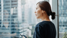 A woman holding a smartphone looks outside a window