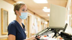 A nurse wearing mask is using a corridor laptop