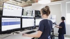 Two people standing before a bank of screens
