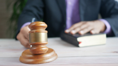 A person holding a gavel with one hand on a book