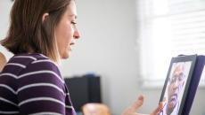A patient holding up a tablet computer is in a virtual consultation with a doctor