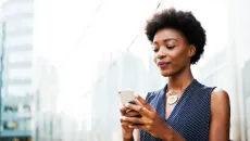 Woman checks her mobile phone next to a building on a city street