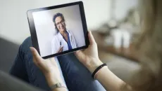 Patient holds a tablet in a telehealth call with her doctor