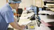 Surgeon in scrubs reviews patient information at a computer terminal 