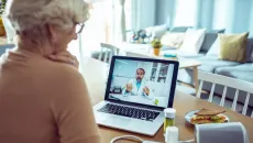 senior woman speaks to her doctor on a laptop at her kitchen table