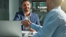 Practice manager shakes hands with a vendor across a desk 