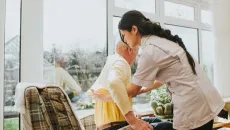Nurse helps a senior patient stand up from a recliner