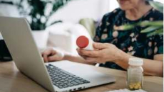 Person holding a pill bottle and using a laptop