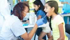 Healthcare worker in mask looking into the mouth of a patient