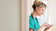 Female doctor in scrubs reviews AI-generated clinical notes on a tablet