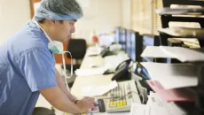 Healthcare worker in scrubs and hairnet using computer