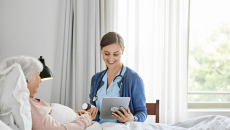 A caregiver holding a digital tablet and checking an elderly patient's medication