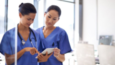 Two nurses checking a patient file on a digital tablet