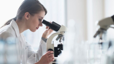Healthcare worker looking through microscope in lab