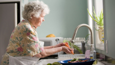 Woman with short hair washes carrots with an electric faucet.