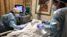 Clinicians in protective gear take care of an ICU patient.