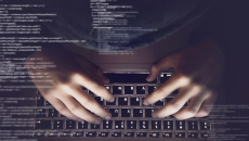 Code appears in the foreground over hands on a laptop.