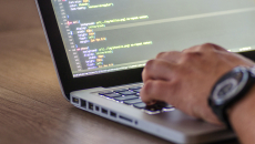 Close-up of a software developer's hand on a laptop with code on the screen