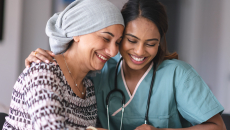 A clinician and a cancer patient with a head scarf smile as they look down.