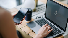 An individual is holding her cell phone and logging into her laptop.