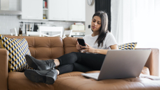 Woman on a couch at home checks her phone to book a doctor's appointment.