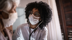 Healthcare worker in mask checking patient in mask with stethoscope