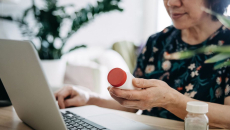 Person holding pill bottle using a laptop