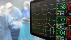 A monitor in the foreground and three surgeons appear in the background.