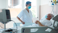 A hospital staff member stands at a patient's bedside.