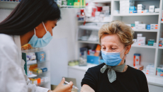 A pharmacist at a retail pharmacy delivers a vaccine to an older woman.