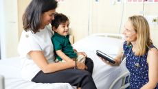 A doctor holding a digital tablet is sitting beside a mother and her child