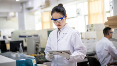 A female healthcare researcher in a lab looks at a tablet.