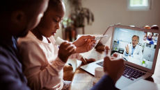 Person with child holding electronic thermometer during telehealth appointment