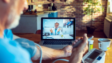 Doctor appears on screen as patient in foreground checks blood pressure at home
