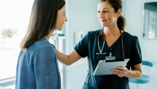 A nurse holding a digital tablet is conversing with a patient