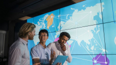 Workers looking at a tablet with world map projected in background