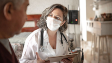 A doctor holding a digital tablet consulting with a senior patient during home visit.