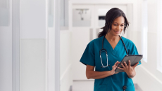 A doctor in scrubs checking a patient's file on a digital tablet