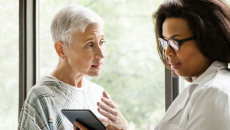 A senior patient consulting with a doctor who is holding a digital tablet