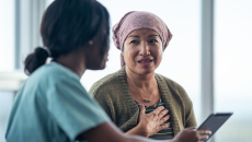 A patient in a headwrap consulting with a doctor who is holding a digital tablet