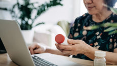 A patient holding a bottle of medicine is in a virtual consultation with a doctor using laptop