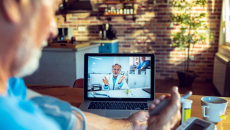 A senior patient is using a blood pressure monitor while consulting with a doctor.
