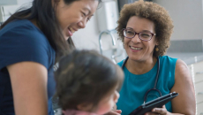 A doctor holding a digital tablet in a consultation with a parent and their child