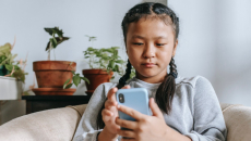 Young person sits on a couch and types on a mobile phone