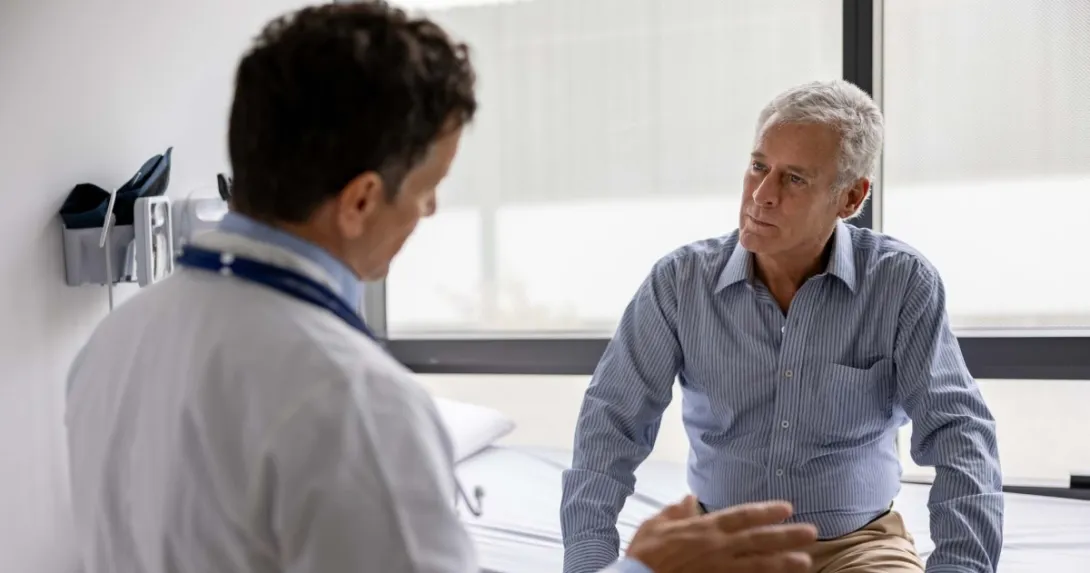 A patient sits on an exam table and listens to the doctor in the foreground talking