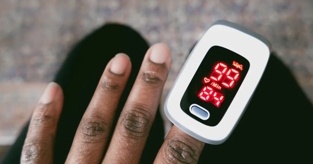 Dark skinned hand with a pulse oximeter measuring the patient's oxygen levels Dark skinned hand with a pulse oximeter measuring the patient's oxygen levels