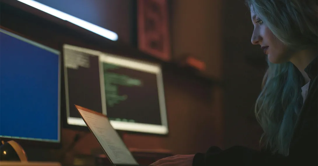 A security IT professional with long hair sits at a desk and monitors a client system remotely A security IT professional with long hair sits at a desk and monitors a client system remotely