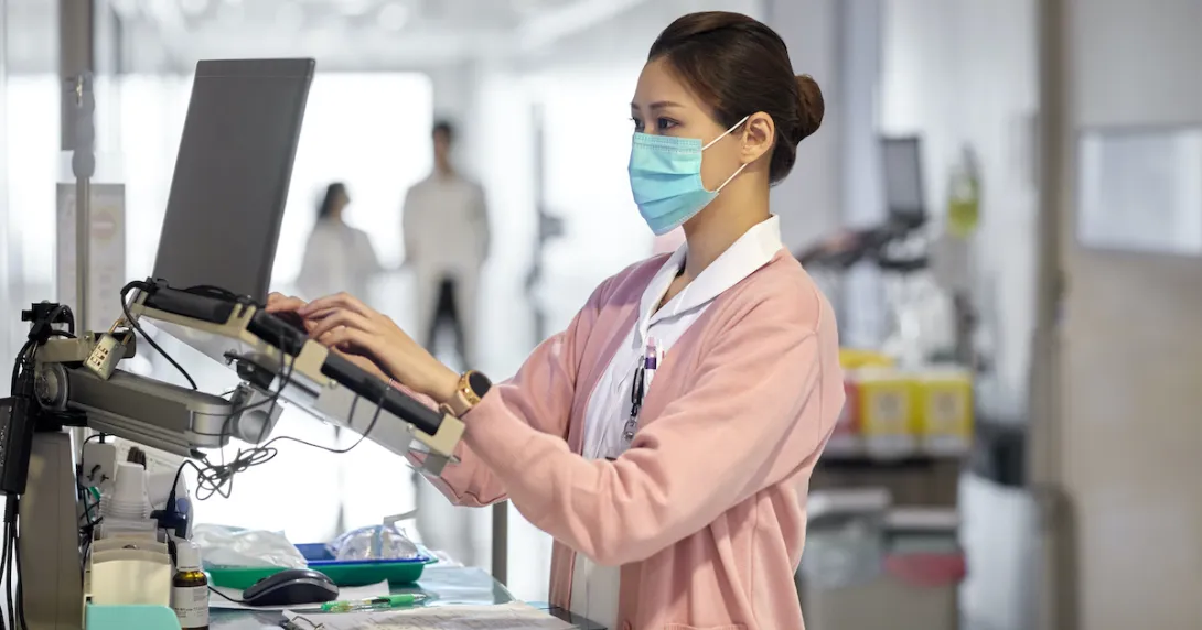 A nurse checking a patient's file on a laptop in the hospital corridor