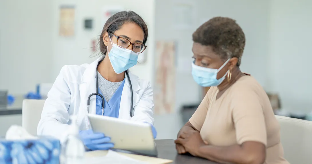 Masked doctor showing tablet to masked patient